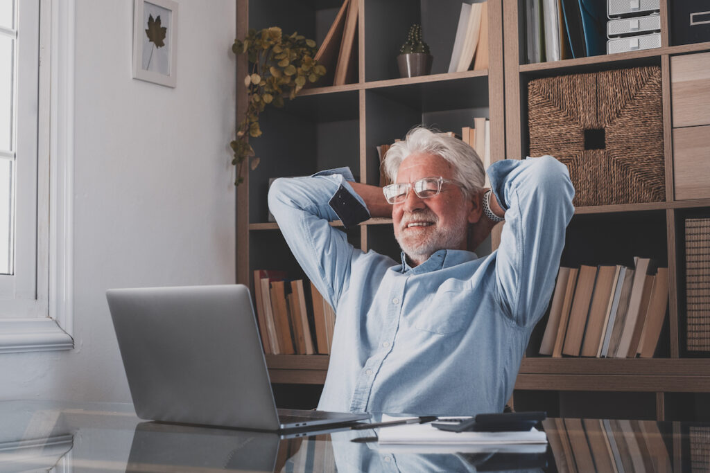 Happy satisfied caucasian mature man rest at home office sit with laptop hold hands behind head